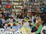 Grupa uczniów gimnazjum siedzi i leży na mteracach na podłodze. Wokól na ścianach regały z książkami.