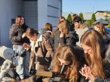 Grupa nastolatków ogladających teleskopy przed okrągłym budynkiem
