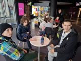 Troje uczniów w kurtkach siedzi przy okrągłym stoliku w lobby kina