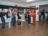 Sześcioro licealistów stoi pośrodku sali, jeded z nich podpiera się o mównicę. Między nimi na sznurkach są czerwone balony...