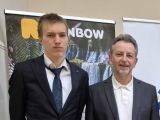 Mężczyzna i nastolatek w garniturach na tle żółto-szarego rollapa.