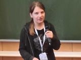 Nastolatka z mikrofonem w ręku, w tle tablica szkolna w sali wykładowej