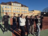 Grupa młodych ludzi na tle żółtego budynku obserwuje niebo