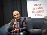 Mężczyzna z mikrofonem na kanapie. W tle napis Mamy w sobie niejedno życie