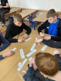 Uczniowie wokół stolika, na którym znajdują się małe kartki papieru