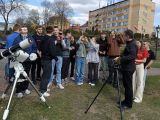 Grupa młodych ludzi na tle żółtego budynku. Na pierwszym planie teleskopy.