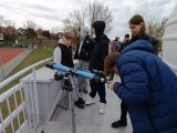 Kilkanaście osób prz teleskopie na dachu budynku astrobazy.