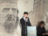 Chłopiec w garniturze przy mównicy na tle portretu Władysława Łokietka