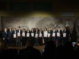 Kilkanaście osób w galowych strojach na tle baneru z Włądysławem Łokietkiem