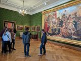 Grupa uczniów w dużej sali zamkowej z zielonymi ścianami. Na ścianach obrazy w złoconych ramach