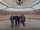 Grupa uśmiechniętych uczniów wewnątrz ogromnego stadionu. W tle biało czerwone siedziska