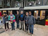 Sześć osób na podziemnej stacji metra. Za nimi czarne wagony podziemnego pociągu
