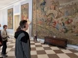 Uczniowie ze słuchawkami na uszach patrzą na arras zawieszony na ścianie