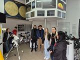 Wnętrze pomieszczenia z przrządami do obserwacji astronomicznych. Grupa kilkunastu osób rozproszonych po pomieszczeniu