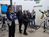 Piecioro ludzi wewnątrz pomieszczenia w przyrządami do obserwacji astronomicznych. Wszyscy stoją i patrzą w jednym kierunku.