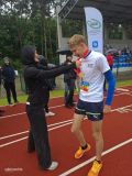 Bieżnia na stadionie. Kobieta w czarnym stroju zakłąda czerwoną smycz chłopcu w sportowym stroju. (1)