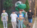 Czterech chłopców w kolorowych t-shirtach. Za nimi model zielonego dinozaura