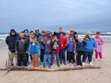 Grupa ludzi w kurtkach na nadmorskiej plaży. W tle wzburzone morze
