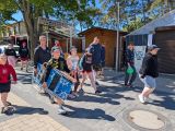 Grupa uśmiechniętych uczniów z plażowymi leżakami idzie nadmorską promenadą