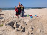 Trzech chłopców i mężczyzna na szerokiej plaży. Przed nimi zamek z piasku