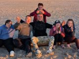 Uśmiechnięty mężczyzna i grupa uczniów siedzi na plaży podczas zachodu słońca