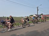 Grupa młodych ludzi na rowerach . W tle pole i zbudowania gospodarskie.