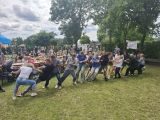 Duża grupa osób stojąca na trawie ciągnie długą linę