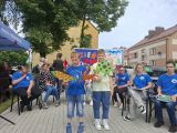 Dwóch chłopców z kartonowymi rekwizytami zwierząt w dłoniach. Za nimi grupa uczniów siedząca na krzesłach