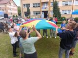 Grupa uczniów tańczy w kole trzymając kolorową chustę