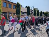 Grupa uczniów maszeruje po ulicy miasta. Z przodu trzy kobiety i chłopak z balonami w dłoni