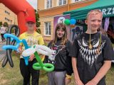 Troje uśmiechniętych uczniów. Dziewczynka w środku z pomalowaną twarzą. Dwoje uczniów trzyma w ręku kolorowe balony