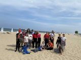 Grupa uśmiechniętych osób na nadmorskiej plaży. Za nimi rozciąga się morze i błękitne niebo