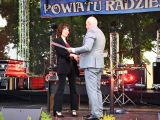 Mężczyzna w szarym garniturze wręcza kobiecie nagrodę na scenie