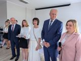 Dwóch mężczyzn w granatowych garniturach. Obok kobiety w strojach galowych