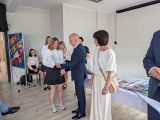 Mężczyzna w granatowym garniturze wręcza świadectwo uśmiechniętej uczennicy. Obok kobieta w jasnej bluzce.