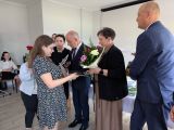 Uczennica w biało-czarnej sukience otrzymuje świadectwo od nauczycieli w strojach galowych