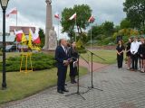 Mężczyzna w garniturze przemawia do zgromadzonych przez mikrofon na te pomnika Łokietka i biało-czerwonych flag.