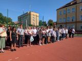 Duża grupa ludzi w strojach galowych na dziedzińcu szkoły