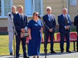 Kobieta w granatowej sukni przemawia przez mikrofon. Za nią czterech mężczyzn w garniturach