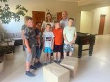 Uśmiechnięty mężczyzna w koszuli i kobieta z długimi włosami. Po prawej i lewej stronie grupa chłopców. Z przodu dwie szare...
