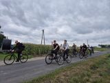 Drogą asfaltową jedzie kilku licealistów na rowerach. Wokół pola i łąki.