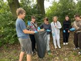 Sześcioro uczniów stoi w kółku. Wszyscy mają niebieskie gumowe rękawiczki i trzymają duży foliowy worek.