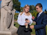 Dwoje uczniów w strojach galowych zapala znicz przed pomnikiem króla