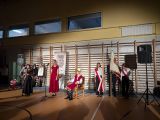 Grupa uczniów w storojach galowych w dużej sali gimnastycznej. W sali nastrojowe, przyciemnione światło. Po prawej poczet...