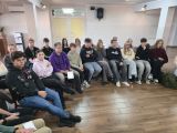W sali w okręgu na krzasłach siedzi duża grupa uczniów liceum. Wszyscy są skupieni i słuchają wypowiedzi innej osoby.