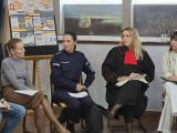 W auli szkolnej na krzesłach obok siebie siedzą cztery kobiety: kobieta w brązowej spódnicy i golfie, policjantka w...