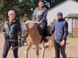 Kobieta i mężczyzna prowadzą jasnego konia. Na koniu uśmiechnięta dziewczyna w kasku
