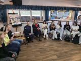 Uczniowie liceum siedzą w kręgu, między uczniami siedzi kobieta w mundurze policyjnym, kobieta w czarnej todze. Rozmawiają.