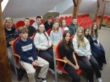 Grupa czternastu licealistów (siedem dziewczyn i siedmiu chłopców) siedzi w sali w trzech rzędach na czerwonych krzesłach.