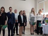Grupa uczniów w strojach galowych. Czworo z nich z mikrofonami w dłoniach
